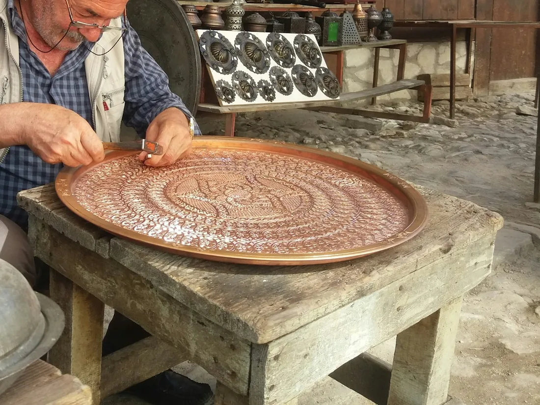 Artesano cincelando un motivo ornamental sobre una bandeja de cobre apoyada en una mesa de taller